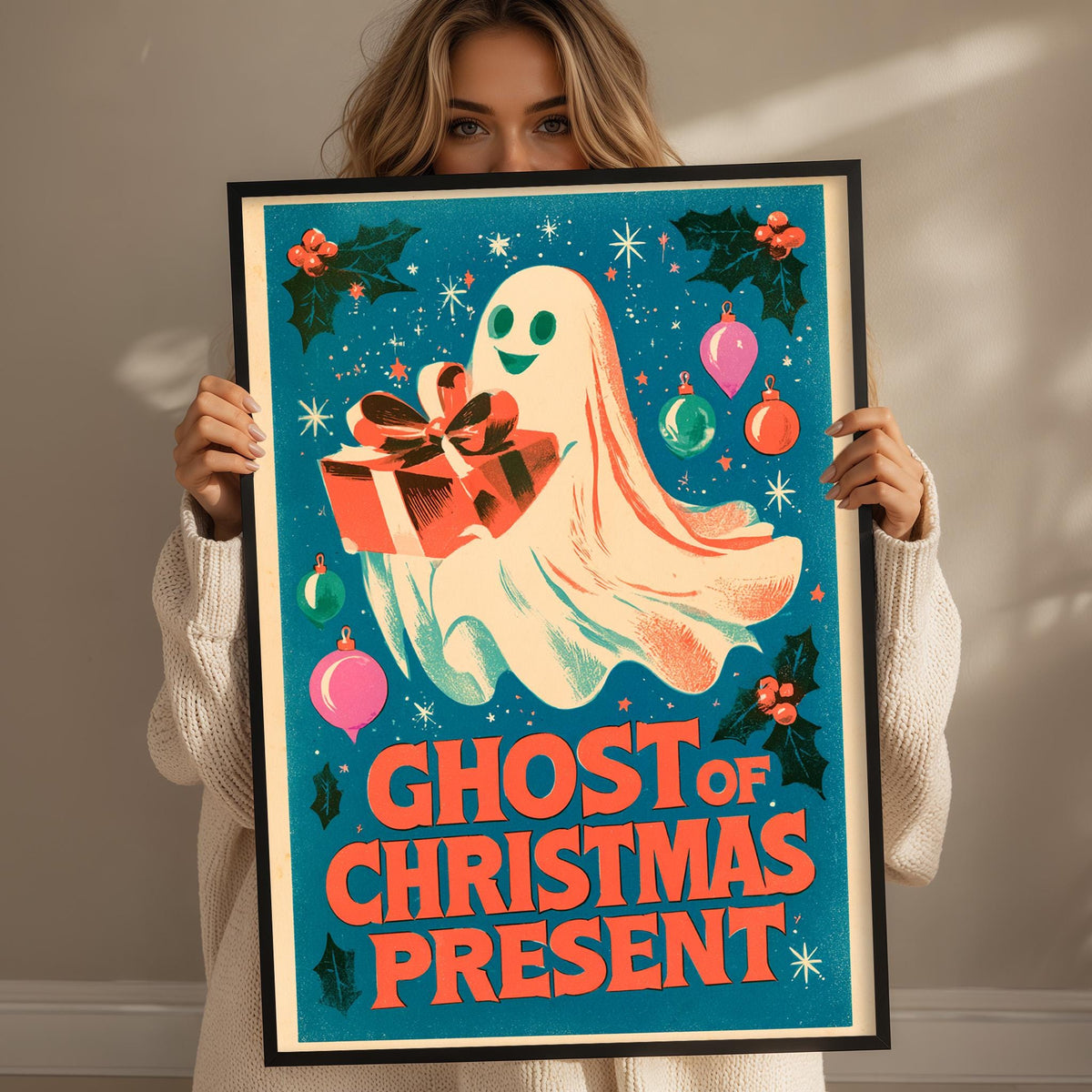 A woman is holding up a framed poster with a ghost and Christmas decorations, including a gift box and holly leaves.