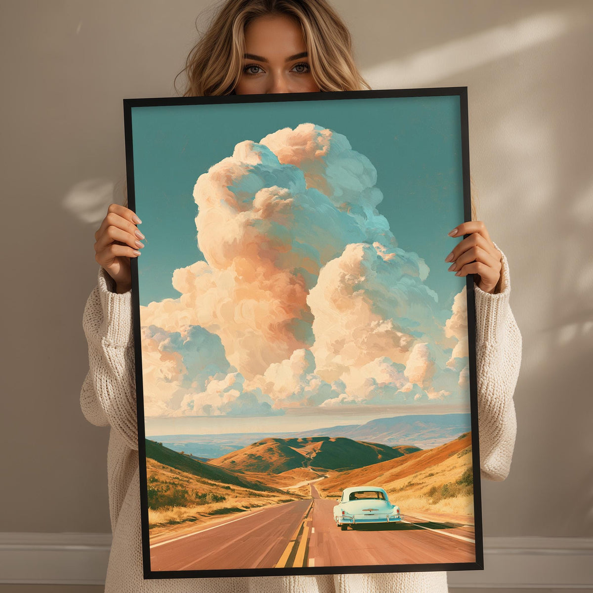 A woman holds up a framed painting depicting a scenic road leading through a mountainous landscape with a blue car traveling along the road.