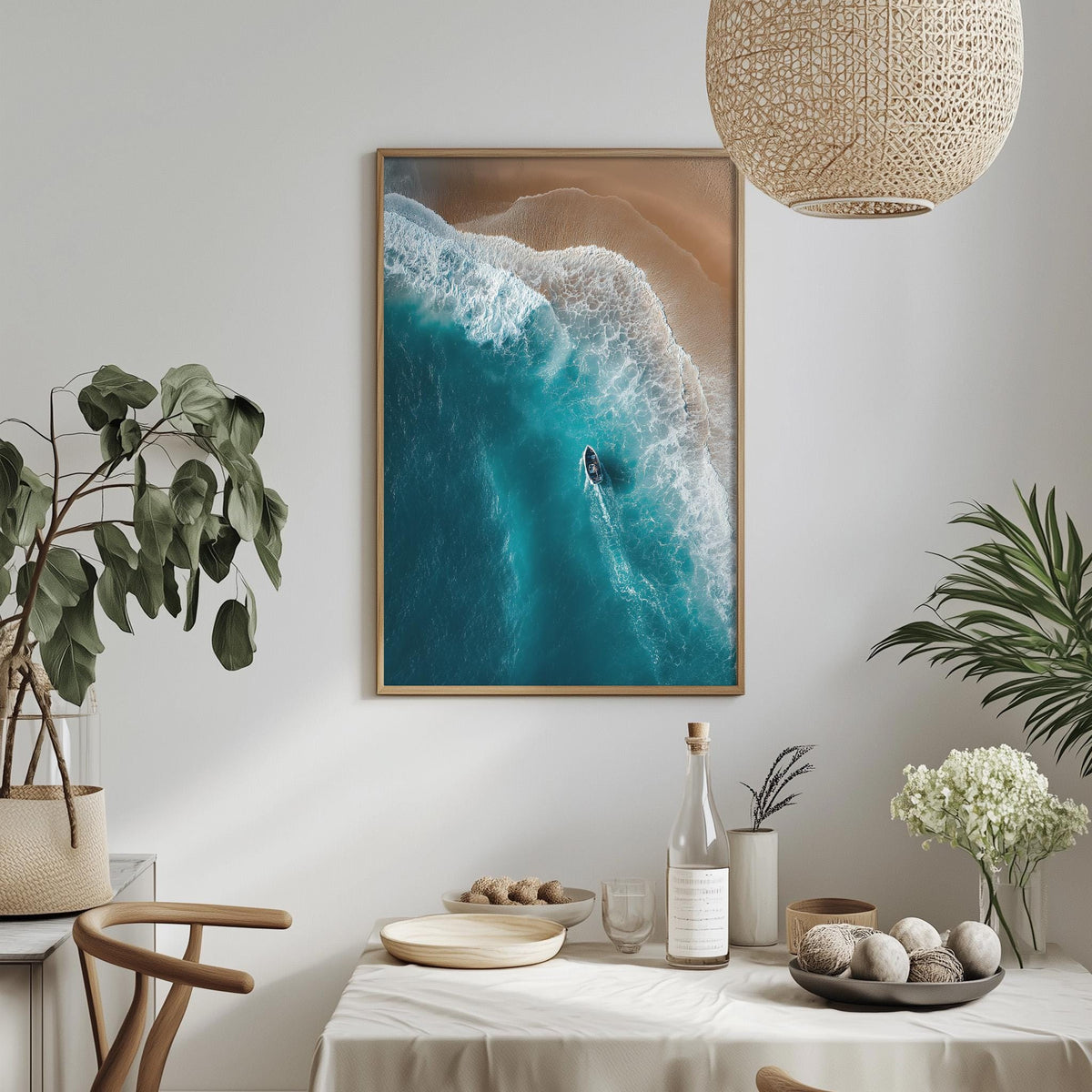 a serene indoor setting with a framed aerial view of a beach scene, a dining table with a bottle, a bowl, and a vase of flowers, and a potted plant.