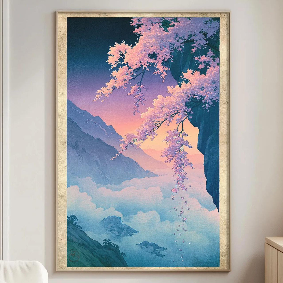 a large framed painting of a serene landscape with mountains, trees, and a colorful sky, hanging on a wall in a living room.