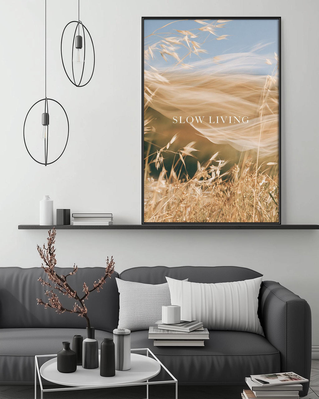 a modern living room with a gray sofa, a coffee table, and a large framed print of a field of wheat with the text "SLOW LIVING" displayed on it.