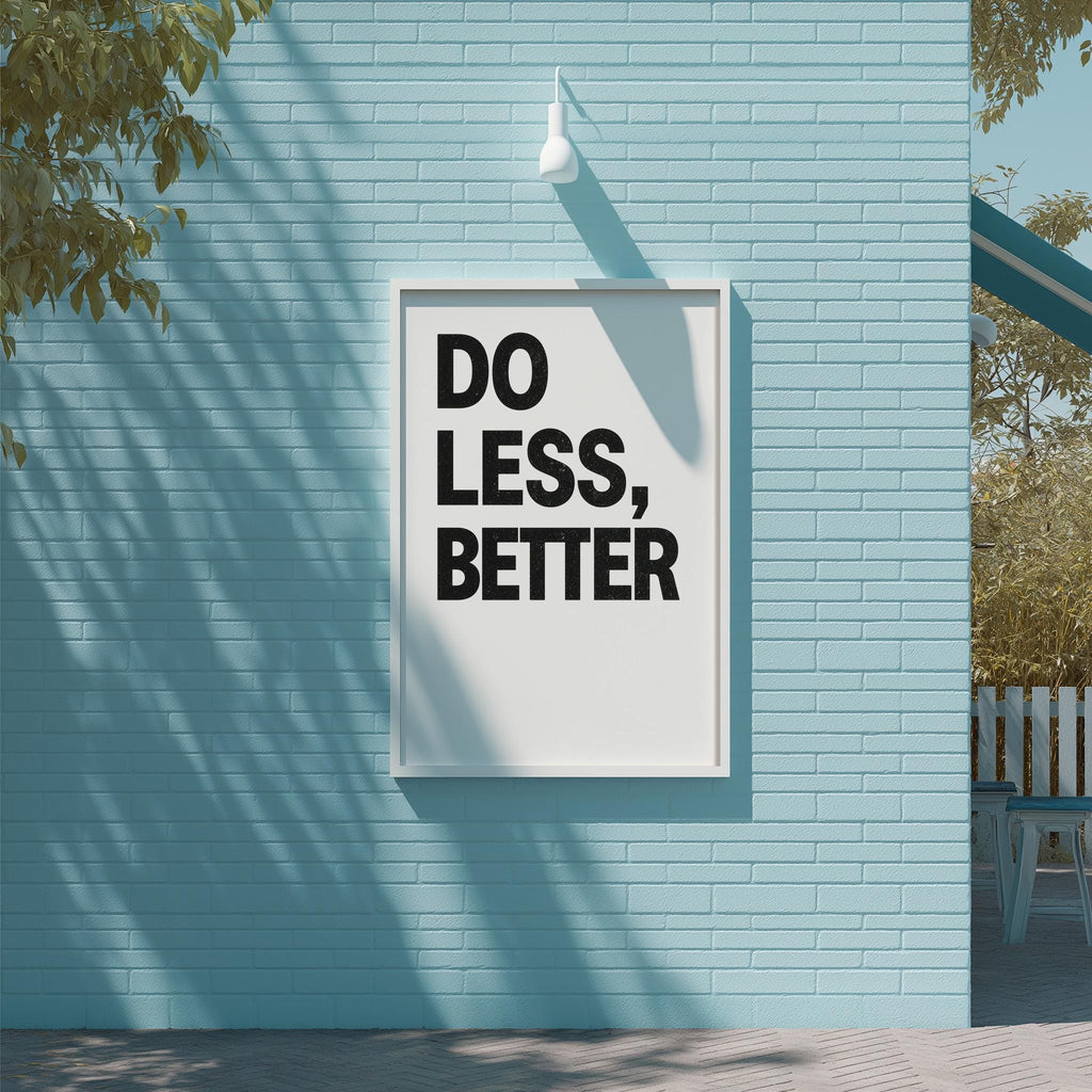 a white sign with the text "DO LESS, BETTER" displayed on a blue brick wall.