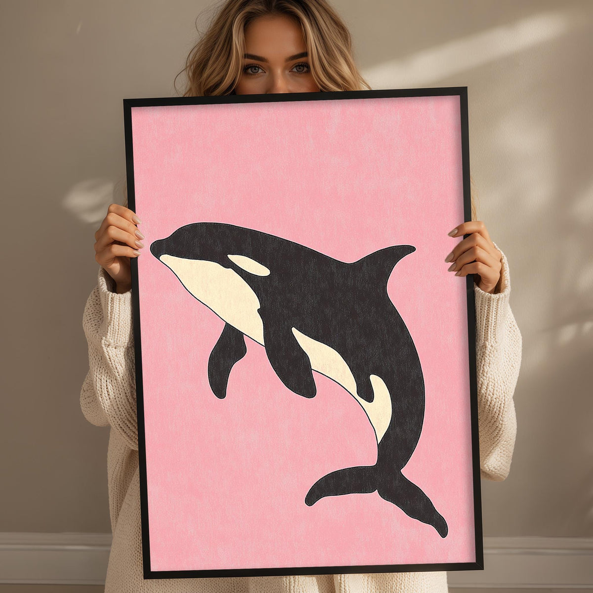 A woman is holding a framed picture of a black and white orca whale in front of her face.