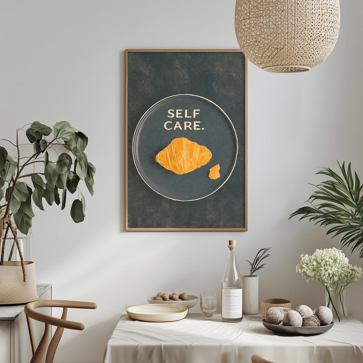 a dining table with a bowl of fruit, a bottle, and a vase, along with a framed poster with a croissant and the text "SELF CARE."