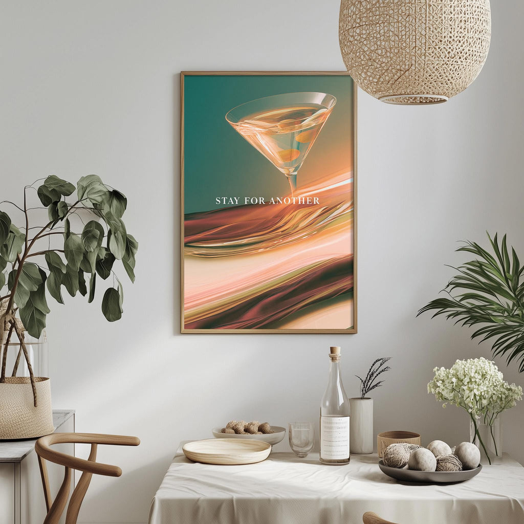 a dining table with a bowl of fruit, a bottle, and a vase, along with a framed poster hanging on the wall above the table.