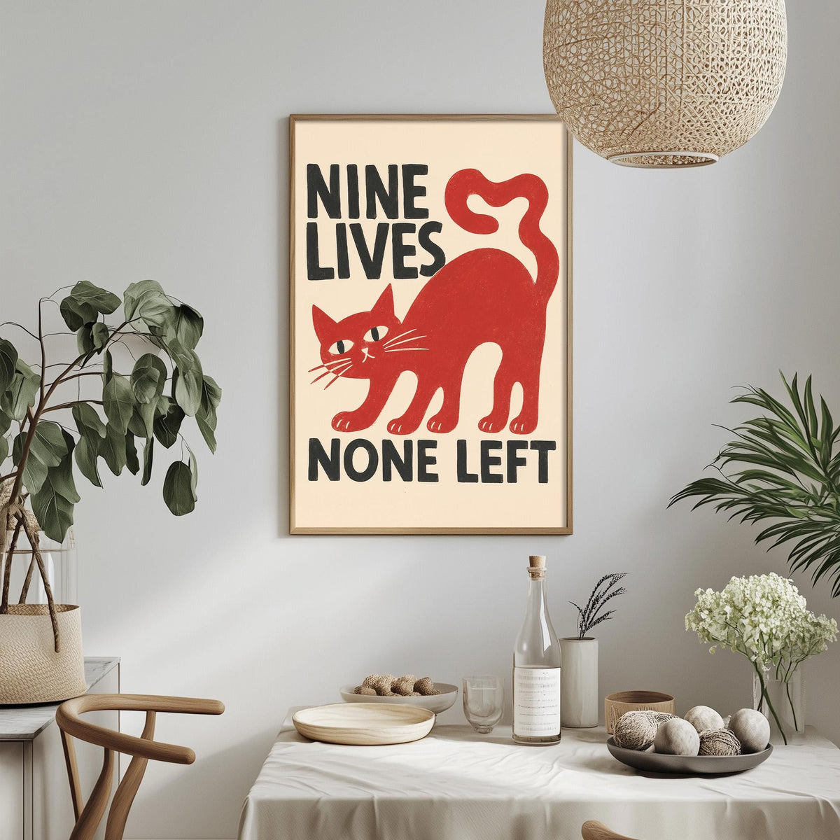 a framed poster with the text "NINE LIVES NONE LEFT" and a red cat illustration, hanging on a wall above a dining table with various items on it.