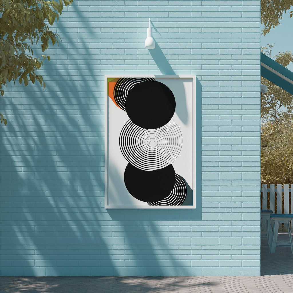 a blue brick wall with a framed abstract artwork hanging on it. The artwork consists of three concentric circles, with the largest circle at the center and the two smaller circles radiating outwards from it. The wall is situated next to a tree, and there is a bench visible in the background.