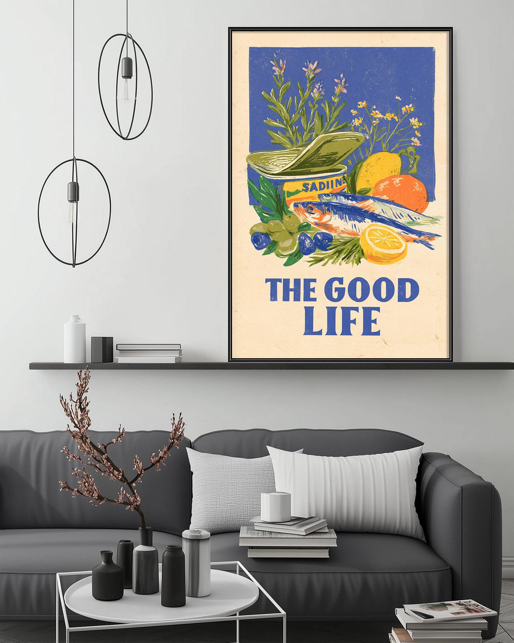 a framed poster with a vibrant illustration of various fruits and vegetables, including oranges, apples, and a bowl, along with the text "The good life". The poster is displayed on a wall above a gray couch, which has a coffee table in front of it. The room also contains a shelf with decorative items and a potted plant.
