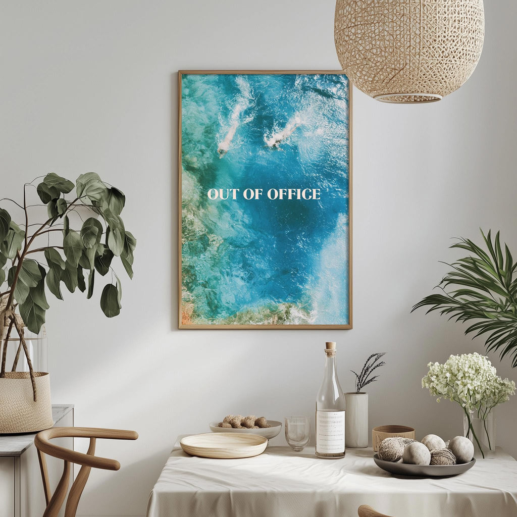 a dining table with a bowl of fruit, a bottle, and a vase of flowers, along with a framed poster hanging on the wall above the table.