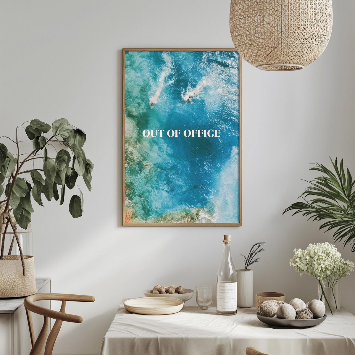 a dining table with a bowl of fruit, a bottle, and a vase of flowers, along with a framed poster hanging on the wall above the table.