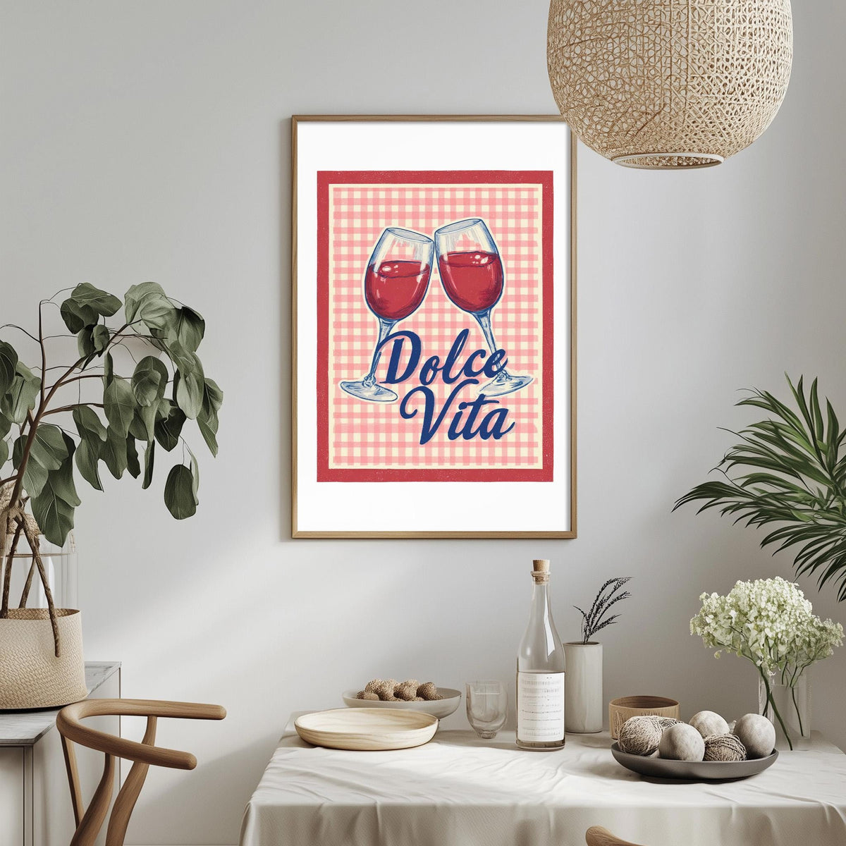 a dining table with a framed poster of two wine glasses and the text "Dolce Vita" above them, along with some decorative elements such as potted plants and a bowl of fruit.