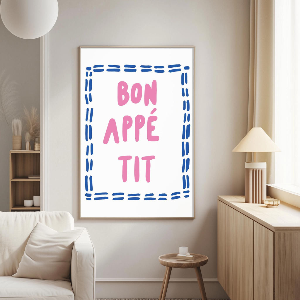 a living room with a white couch, a wooden side table, and a framed poster with the text " bon appe tit" in pink and blue.