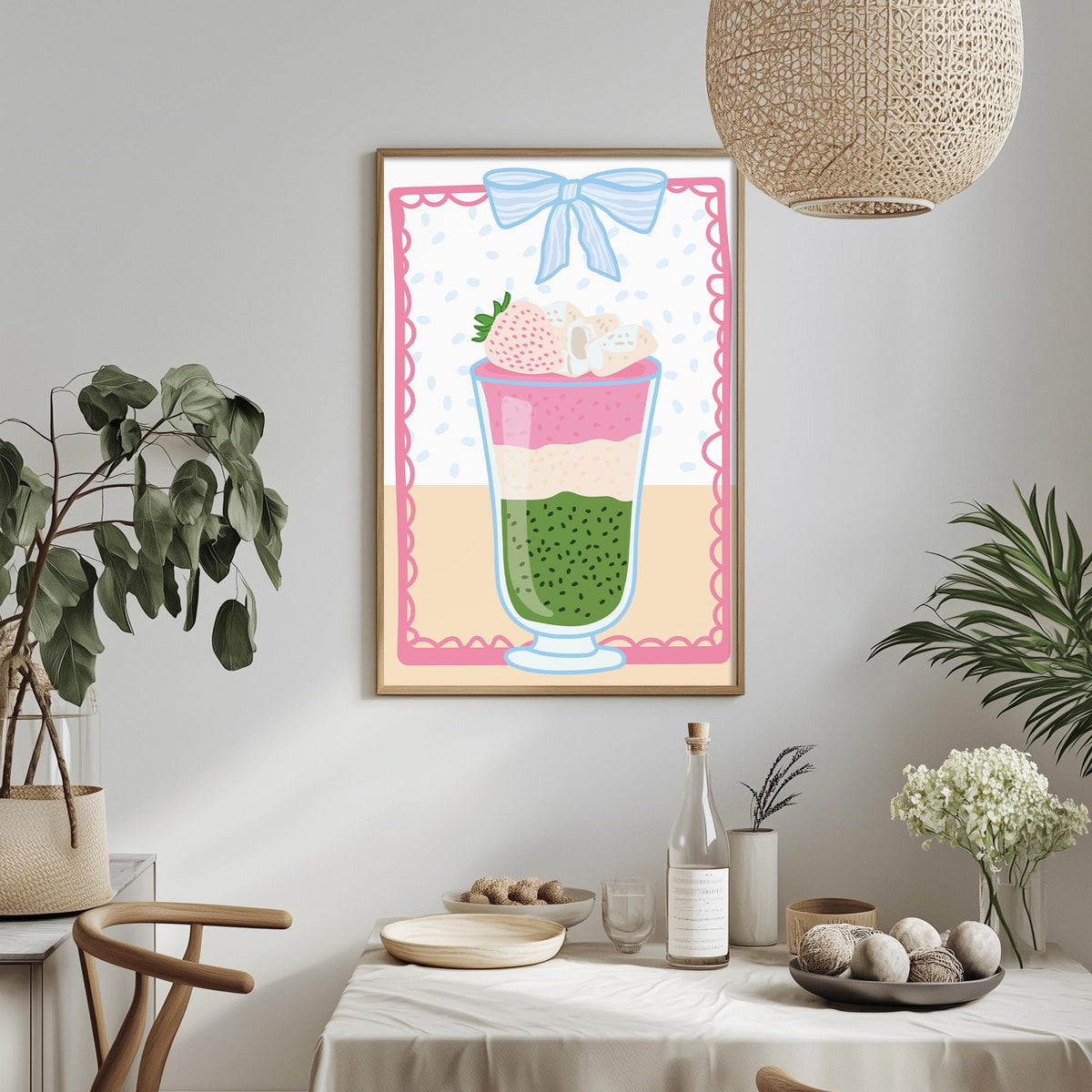 a dining table with a white tablecloth, a bowl of fruit, a bottle, and a vase with flowers. Above the table, there is a framed picture of a layered dessert with a bow on top.