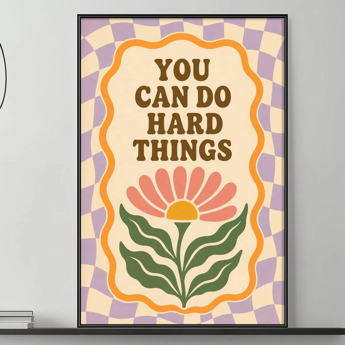 a poster with the text "YOU CAN DO HARD THINGS" displayed on a wall above a gray couch with a coffee table in front of it.