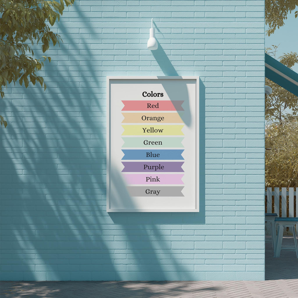 A framed poster on a blue brick wall displaying a color spectrum with the words "Colors Red Orange Yellow Green Blue Purple Pink Gray" arranged in a visually appealing manner.