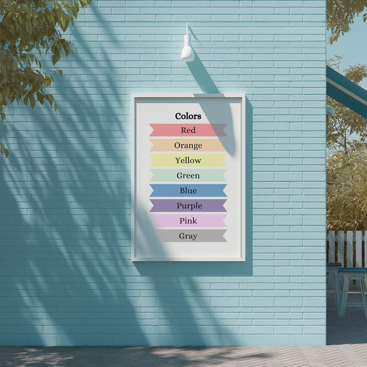 A framed poster on a blue brick wall displaying a color spectrum with the words "Colors Red Orange Yellow Green Blue Purple Pink Gray" arranged in a visually appealing manner.