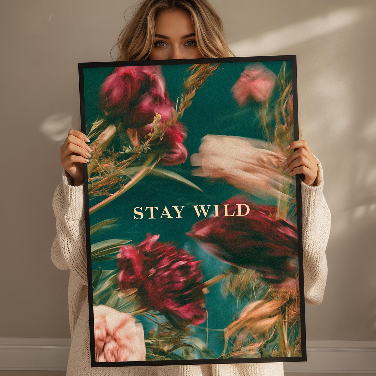 A woman holding a framed poster with a floral design and the text "STAY WILD" on it.