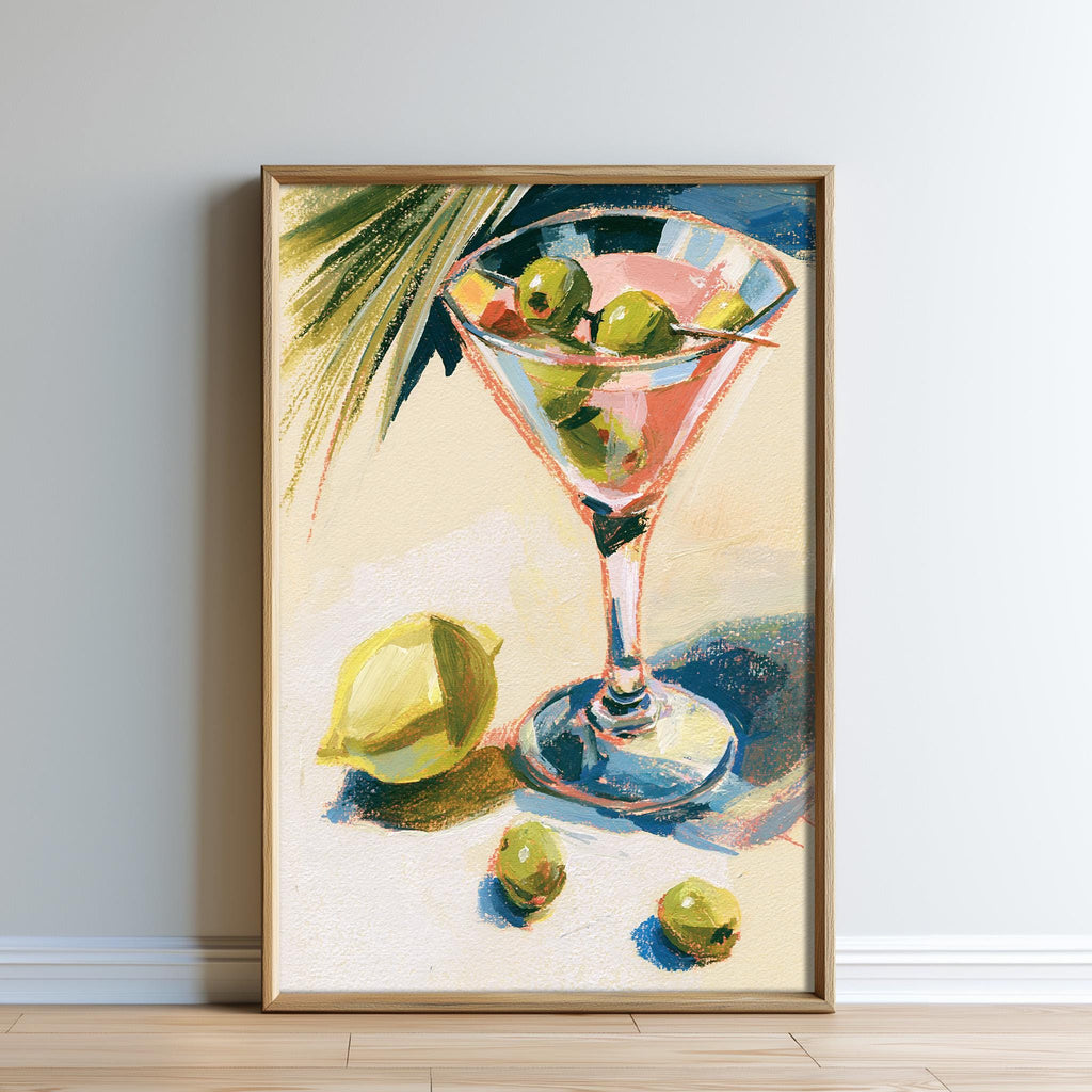 A framed painting depicting a martini glass filled with green olives, placed on a table with a lemon and additional green olives.