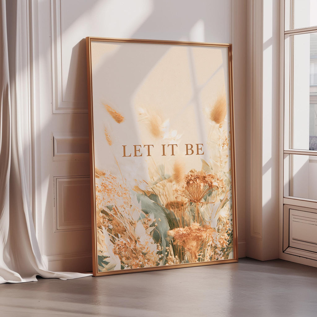 A framed poster with a floral design and the text "LET IT BE" is displayed on a wall in a room with sunlight streaming in from a window.
