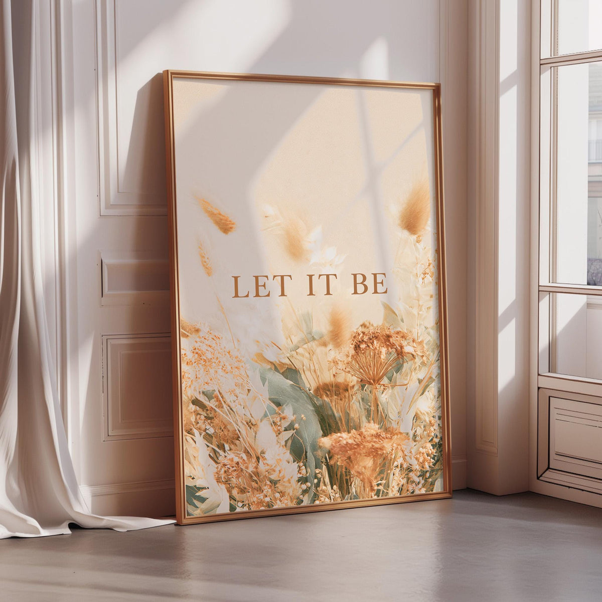 A framed poster with a floral design and the text "LET IT BE" is displayed on a wall in a room with sunlight streaming in from a window.