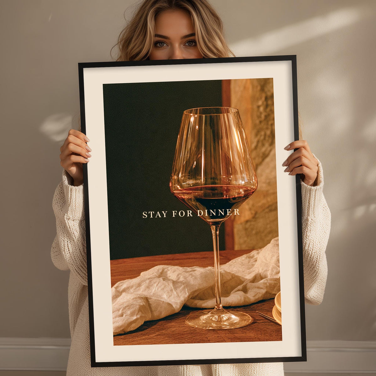 A woman holding a framed picture of a wine glass with the text "STAY FOR DINNER" on it.