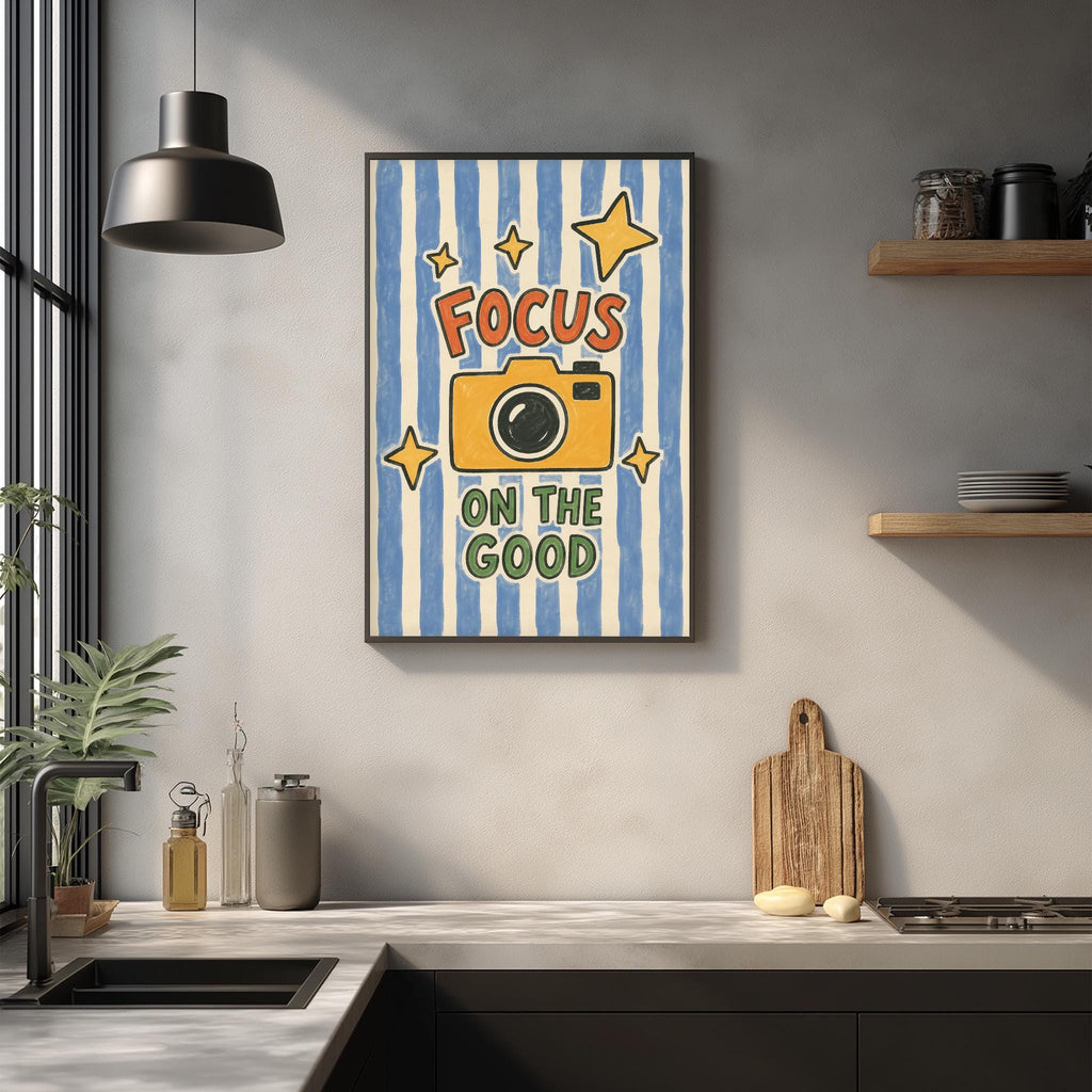 a kitchen counter with a framed poster that reads "Focus on the good" above it. The poster has a yellow camera and stars, and the phrase "Focus on the good" is written in bold letters.