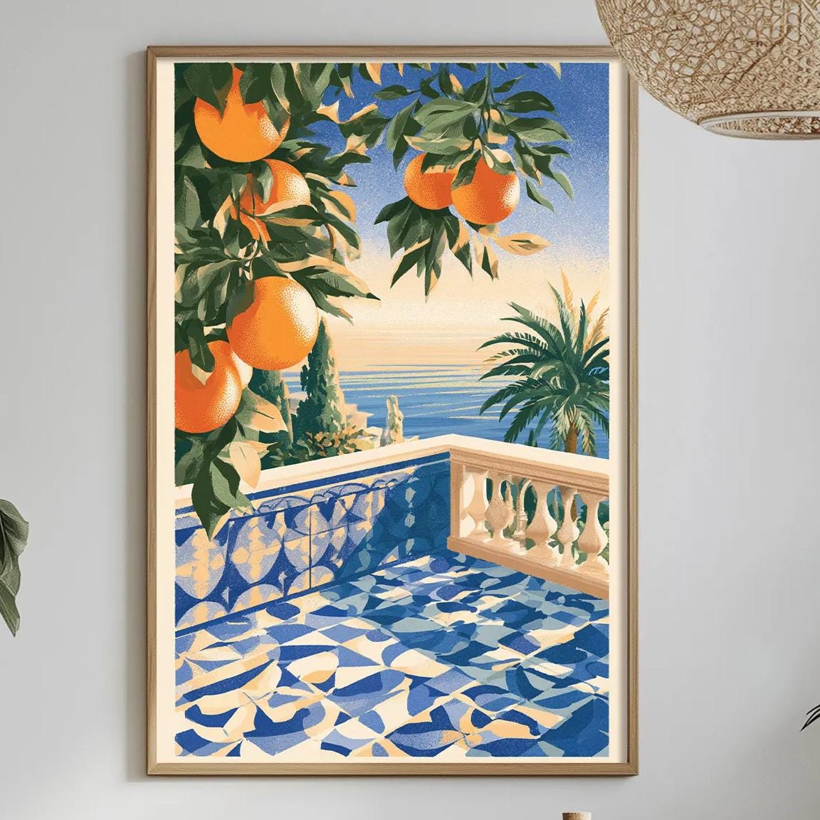 a dining table with a bowl of fruit, a bottle, and a vase of flowers, set against a white wall with a framed painting of a balcony overlooking the ocean.
