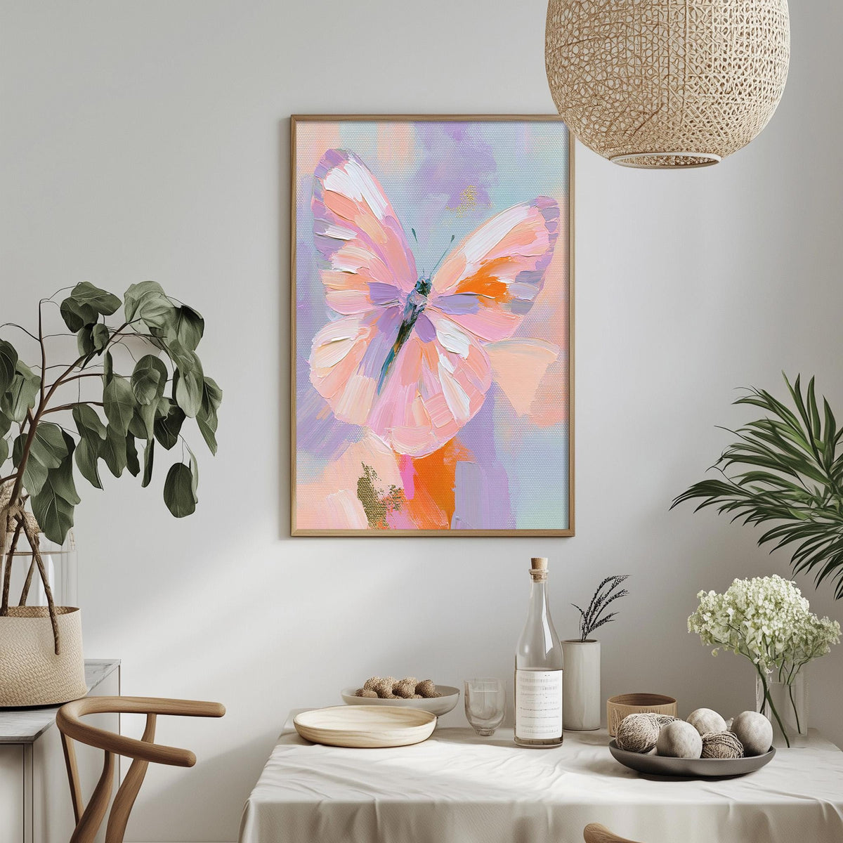 a dining table with a white tablecloth, a vase of white flowers, a bottle, and a bowl of fruit. Above the table, there is a framed painting of a butterfly in pink and orange hues.