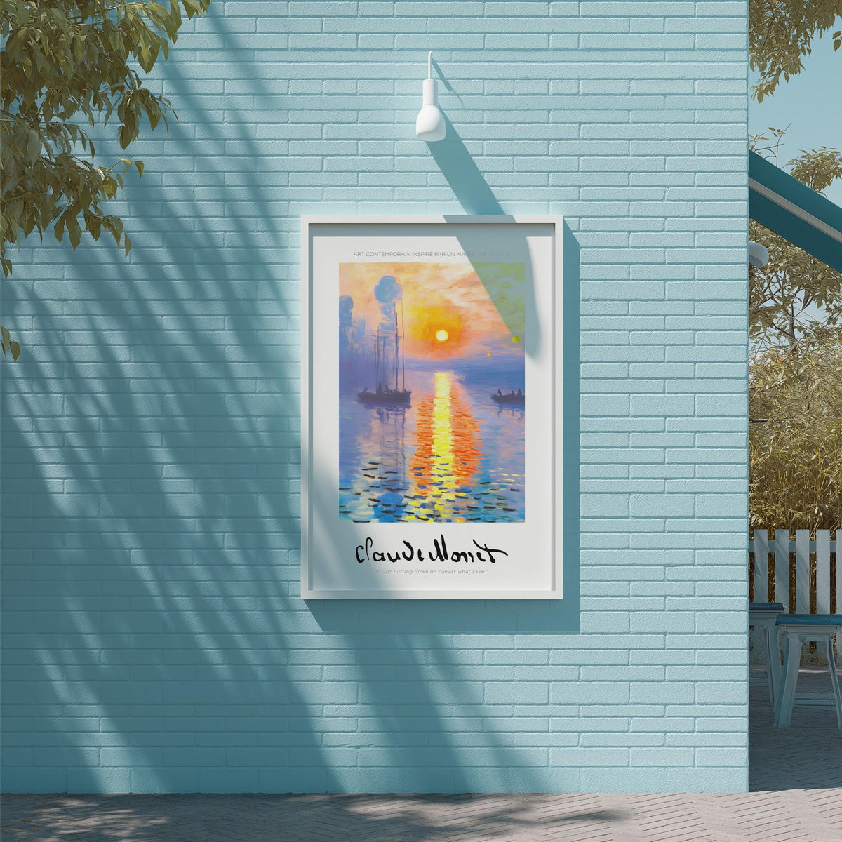 A framed poster of a sunset over a body of water is displayed on a blue brick wall, with a white light fixture above it.