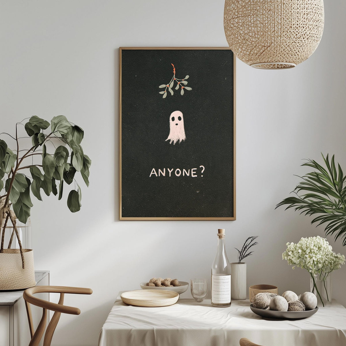 a dining table with a bowl of fruit, a bottle, and a vase of flowers, along with a framed poster of a ghost above the table.