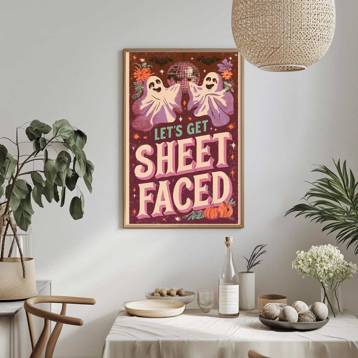 a framed poster with a Halloween-themed design hanging on a wall above a dining table. The poster has a playful and spooky design with ghostly figures and a disco ball. The table is set with various items, including a bottle, a bowl, and a vase, creating a festive atmosphere.
