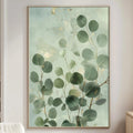 a living room with a large framed painting of green leaves hanging on the wall. The painting is positioned above a white couch, which is placed against the wall. The room also includes a small table and a lamp, creating a cozy and inviting atmosphere.