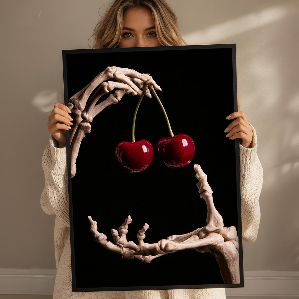 A woman holds a framed image of a skeleton hand holding two cherries.