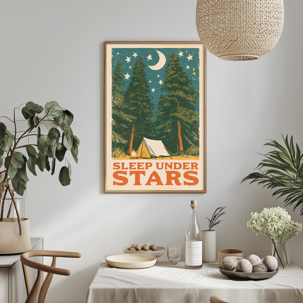a framed poster with a nighttime scene of pine trees and a crescent moon, along with the text "SLEEP UNDER STARS" displayed on the poster.