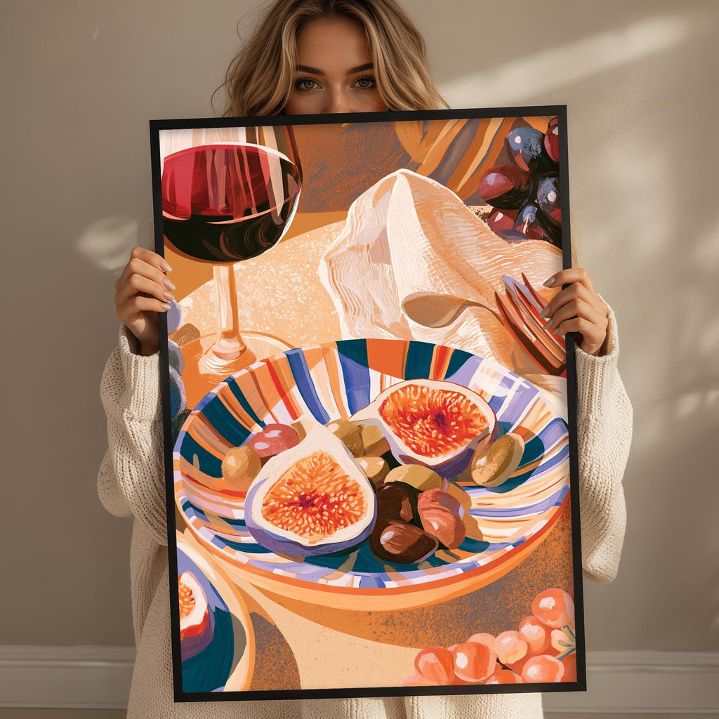 A woman holds up a framed illustration of a table with a wine glass, a bowl of fruit, and a plate of food.