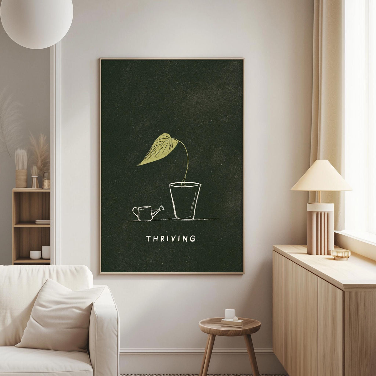 a living room with a large framed poster on the wall that says "THRIVING" in white text. The poster depicts a plant with a green leaf and a watering can, suggesting a connection to nature and growth. The room also includes a white couch, a wooden side table, and a lamp, creating a cozy and inviting atmosphere.