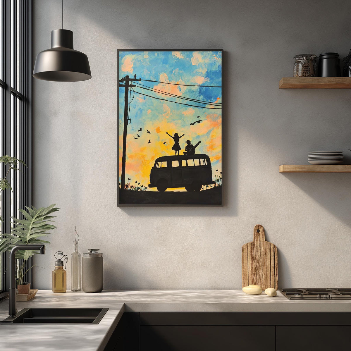 a kitchen counter with various items on it, including a framed painting of a van with silhouettes of people on top, a hanging light fixture, and a wooden cutting board.