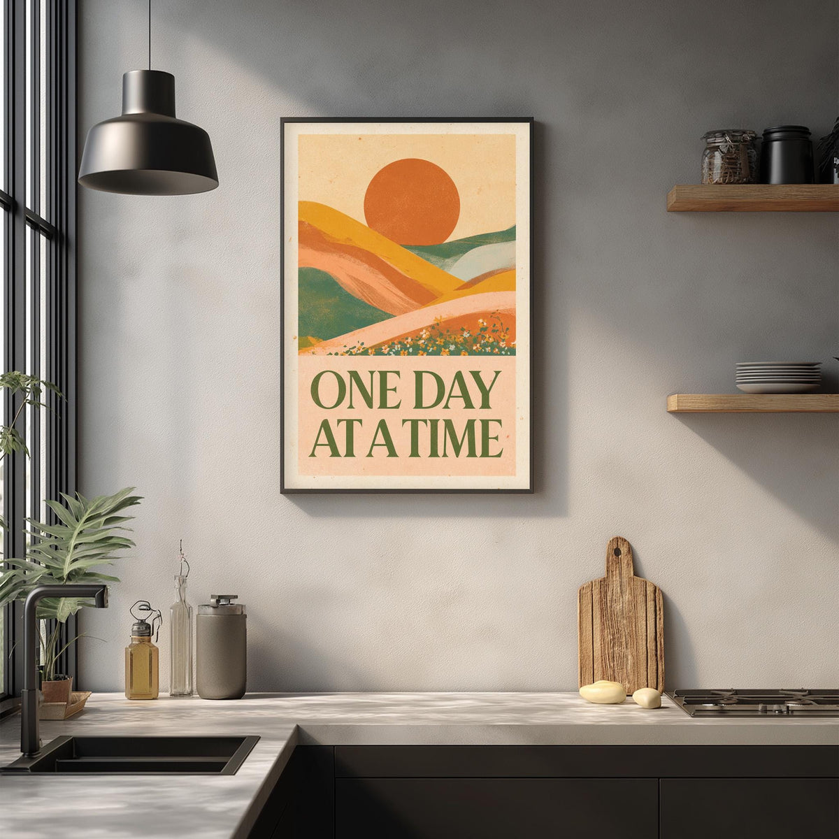 a framed poster with a landscape scene and the text "ONE DAY AT A TIME" hanging on a wall above a kitchen counter with various kitchen items and a cutting board.