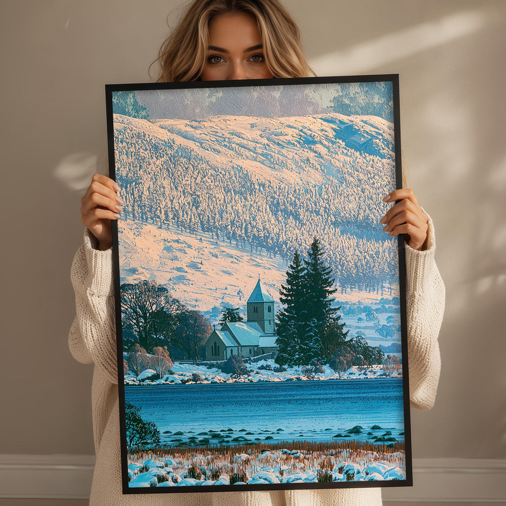 A woman holds up a framed picture of a snowy landscape with a church in the background.
