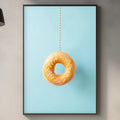 a kitchen counter with a framed picture of a donut hanging on the wall above it. The kitchen counter has various items on it, including a cutting board, a bottle, and a plant.