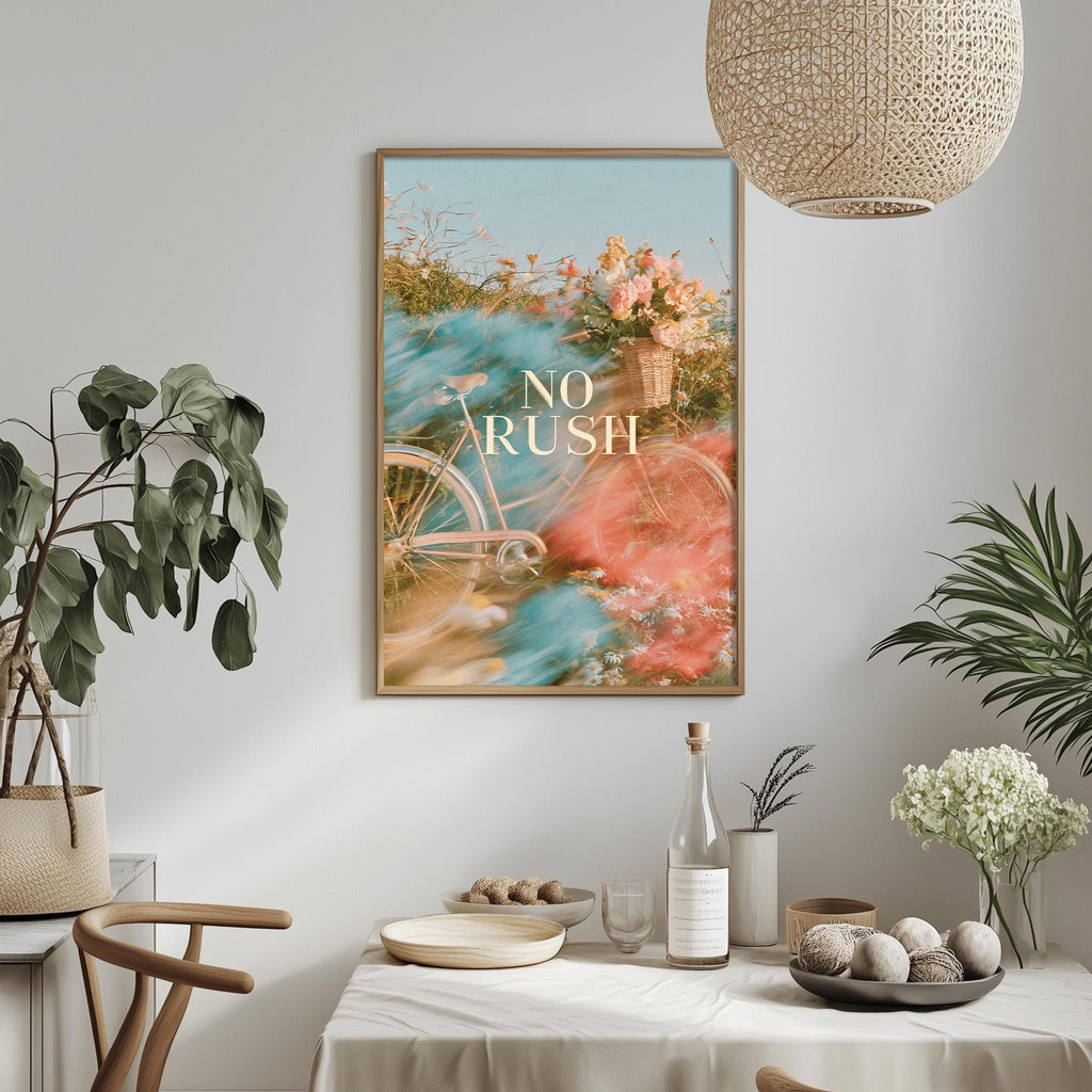 a dining table with a white tablecloth, a bowl of fruit, a bottle, and a vase with flowers. Above the table, there is a framed poster with a bicycle and flowers, and a hanging light fixture.