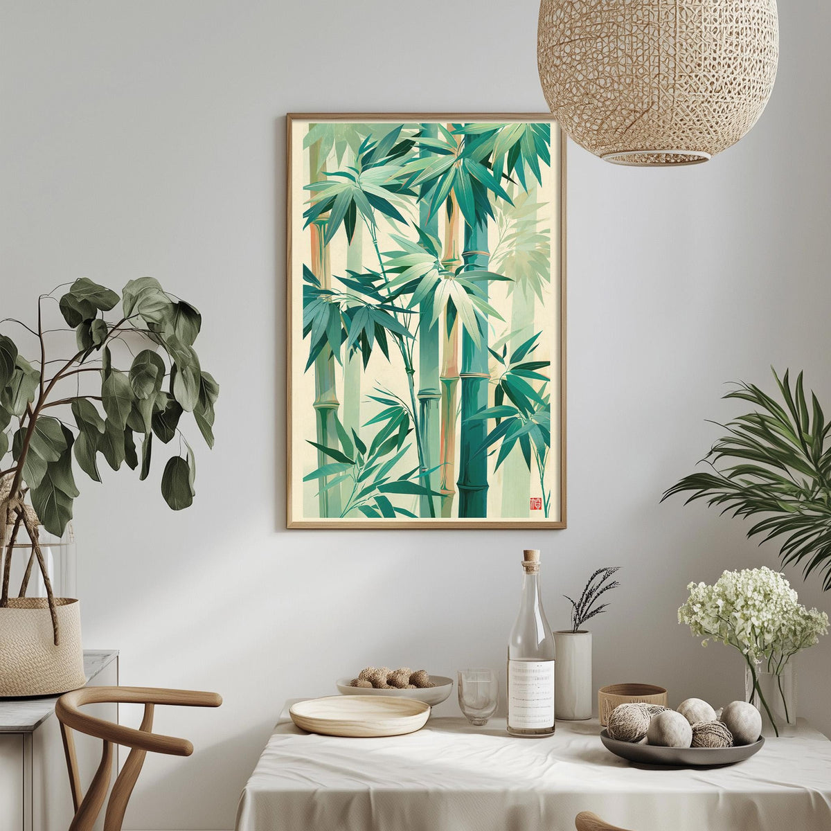 a dining table with a white tablecloth, a bowl of fruit, a bottle, and a vase with flowers. Above the table, there is a framed picture of a bamboo forest with green leaves and brown stems.