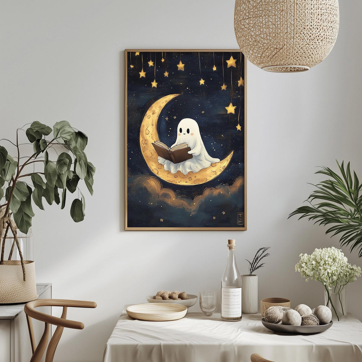 a framed illustration of a ghost reading a book on a crescent moon, surrounded by stars, with a table set for a meal in the foreground.