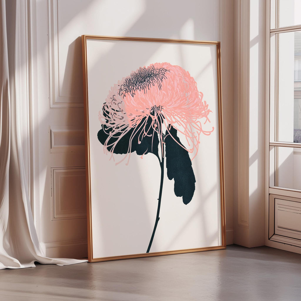 A framed print of a pink flower with black petals is displayed on a white wall in a room with a window.