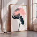 A framed print of a pink flower with black petals is displayed on a white wall in a room with a window.