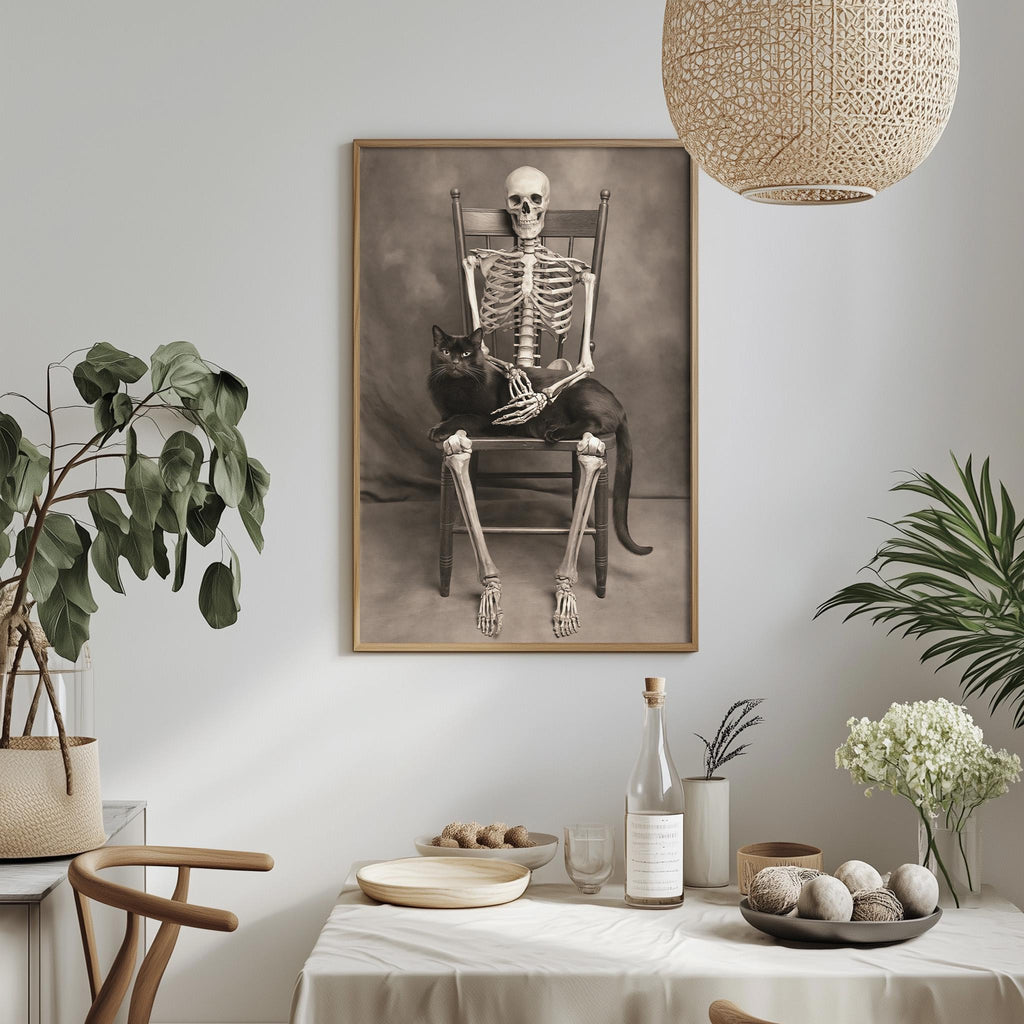 a framed black and white photograph of a skeleton sitting in a chair, holding a cat, with a dining table and various decorative items in the foreground.
