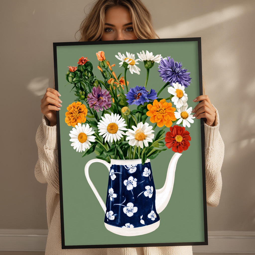 A woman holds up a framed painting of a blue and white teapot filled with a colorful bouquet of flowers.