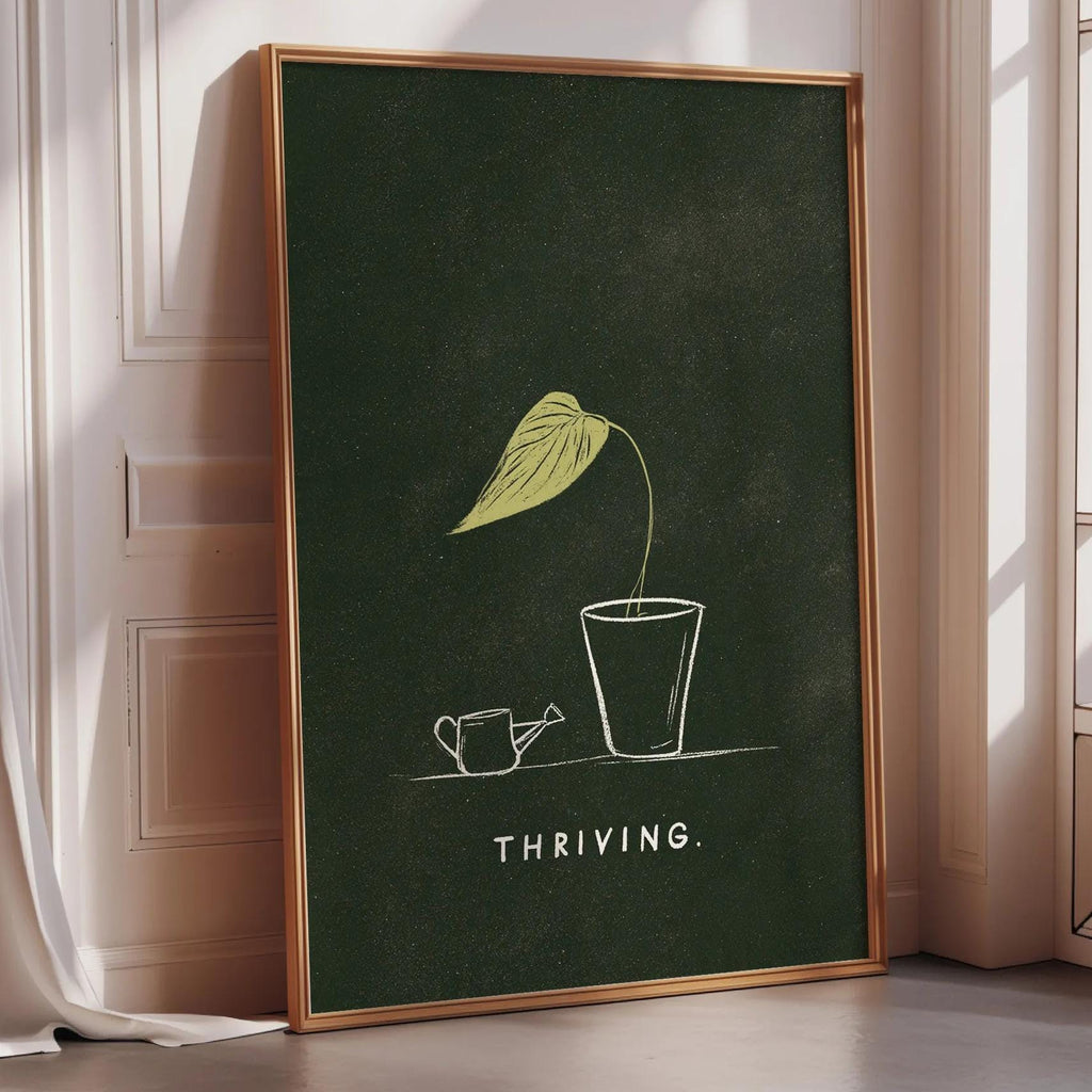 A framed poster with a green background and a yellow leaf illustration, along with the text "THRIVING" below the leaf.