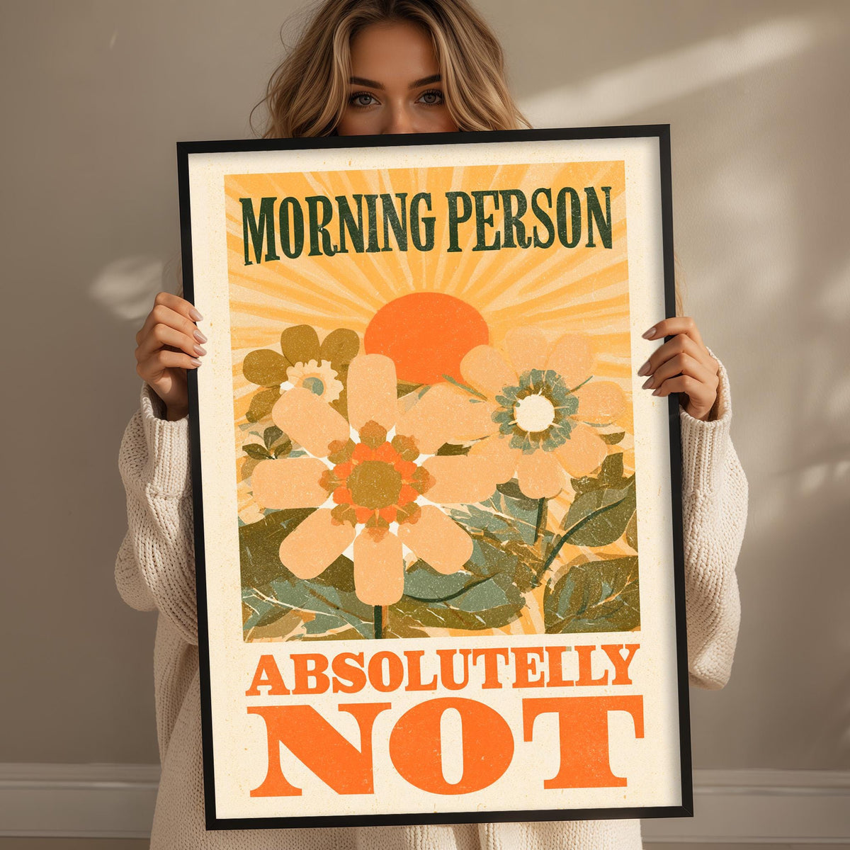 A woman holding a framed poster with a floral design and the text "MORNING PERSON ABSOLUTELY NOT".