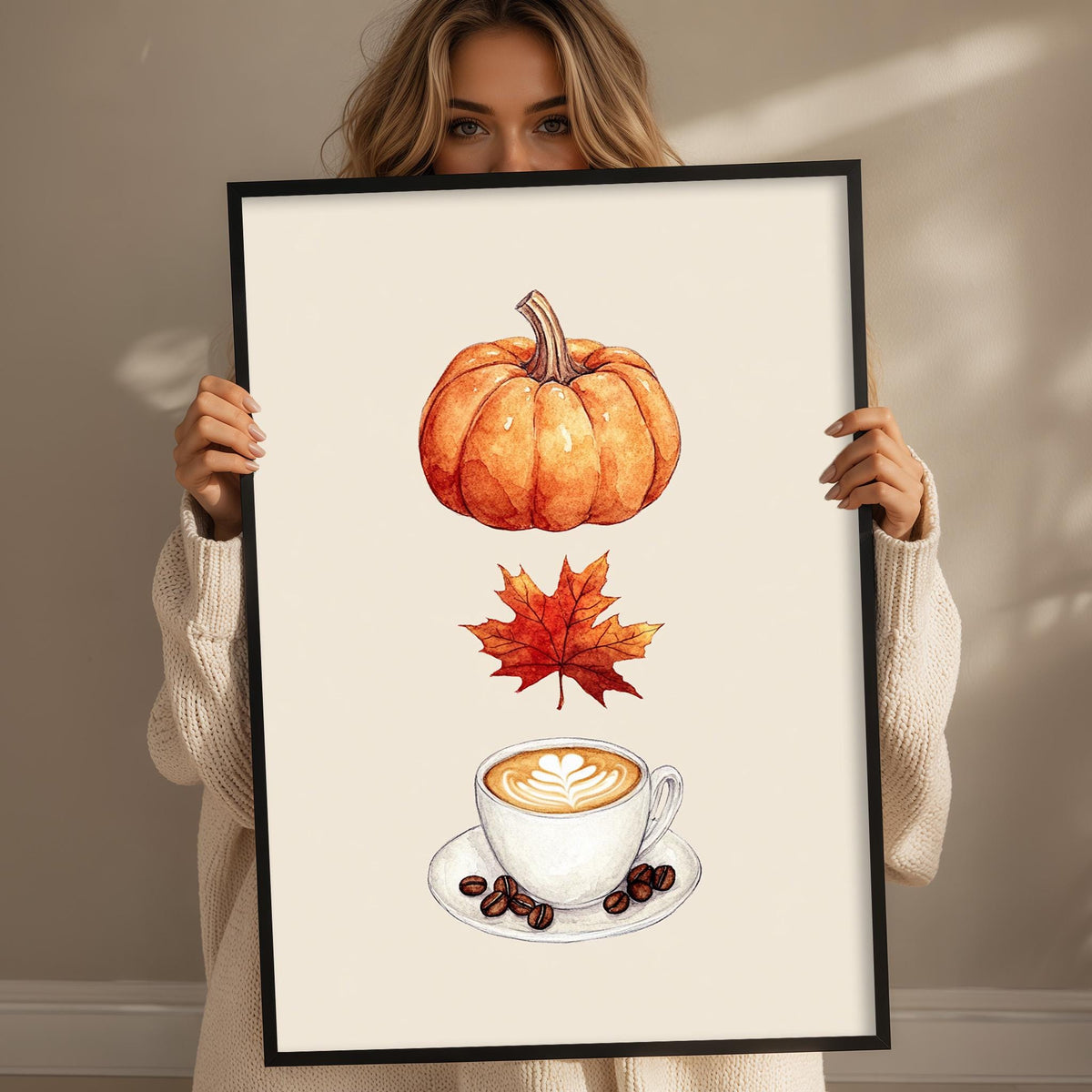 A woman holds up a framed print with an illustration of a pumpkin, a maple leaf, and a cup of coffee.